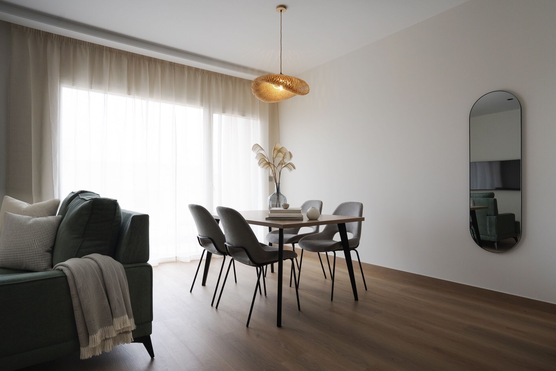 Ein modernes Wohnzimmer mit Essbereich, mit Holzboden, einer Couch, einem Esstisch mit Stühlen, einer Pendelleuchte und einem Spiegel an der Wand.