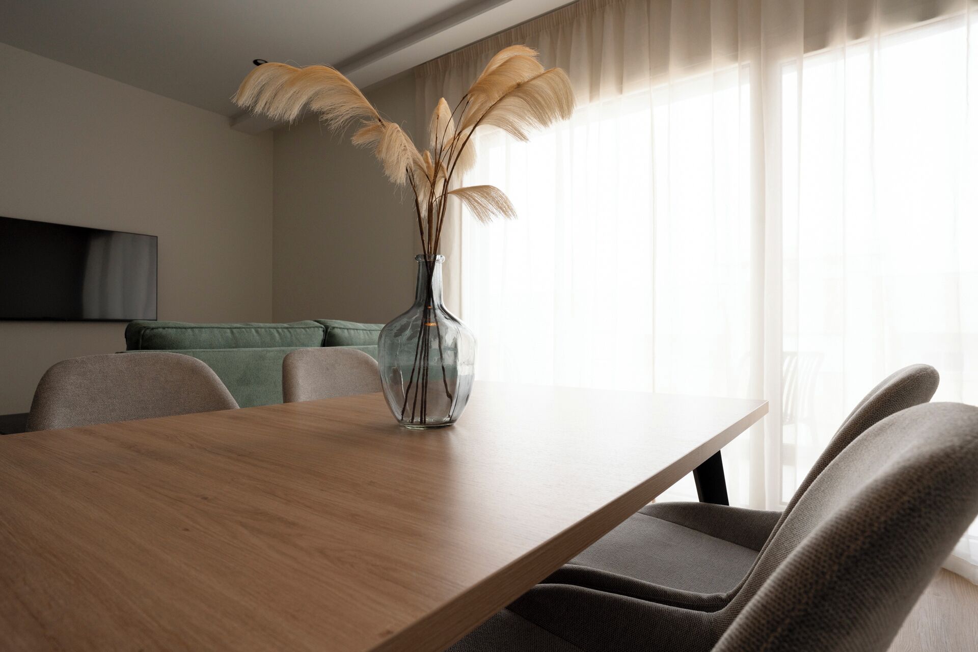 Un comedor moderno con una mesa de madera, un jarrón con plumas de pampa y un sofá verde.