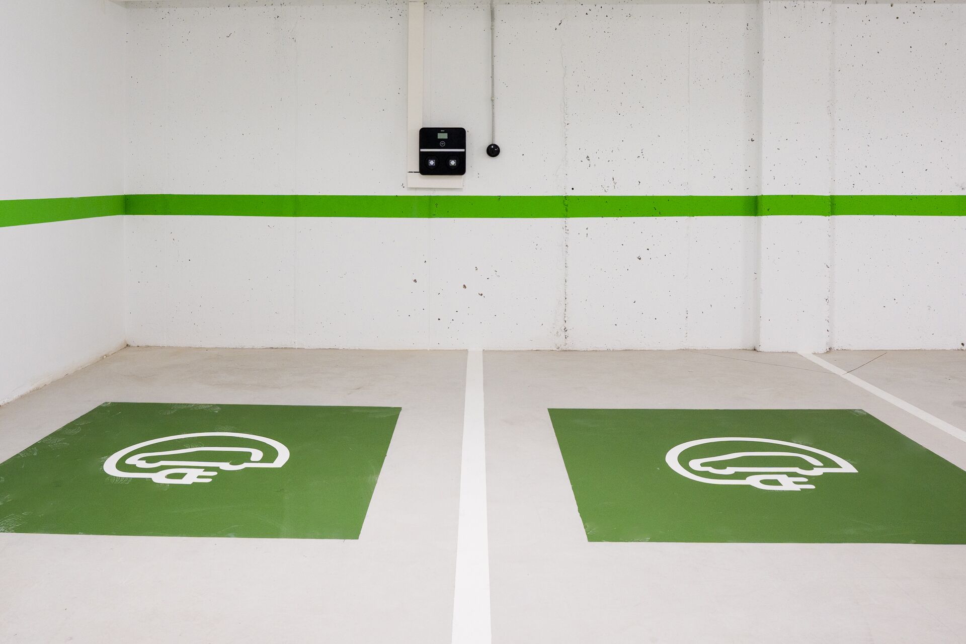 A parking garage with two green parking spaces marked with a white logo.