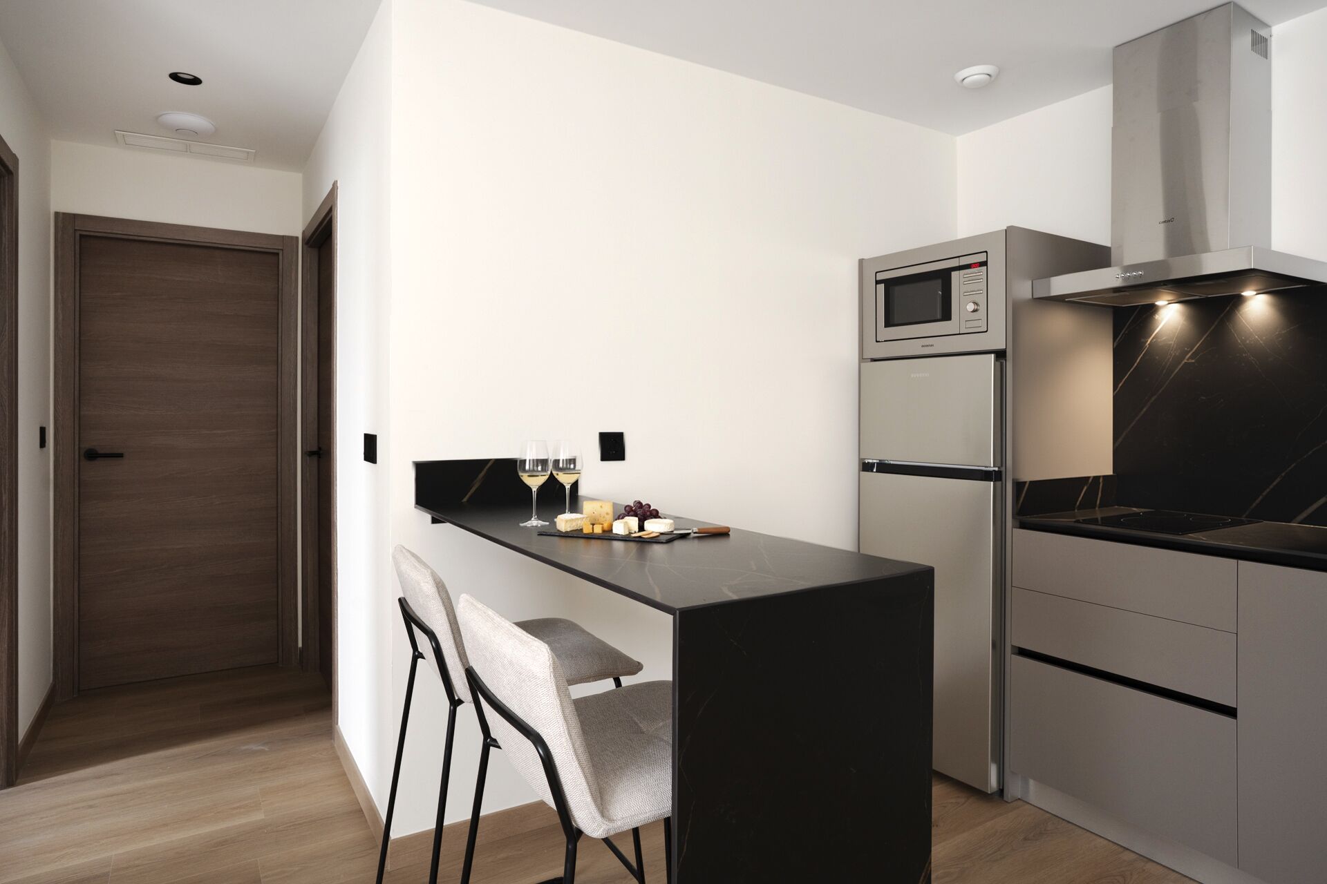 A compact kitchen with a built-in microwave, oven, and stove, a small bar area with a chair, and a door leading to another room.