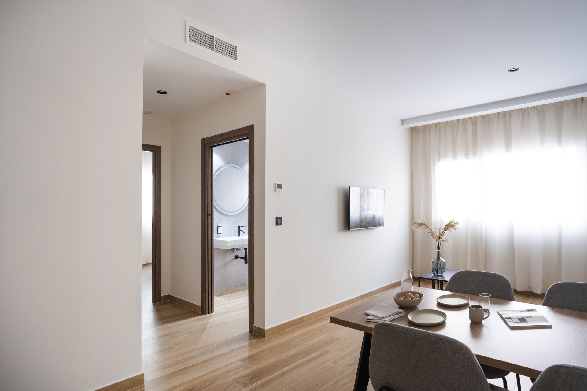 A modern dining area with a wooden table, chairs, and a view of a bathroom through an open door.
