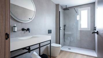A modern bathroom with a large round mirror, two sinks, a toilet, and a glass-enclosed shower area.