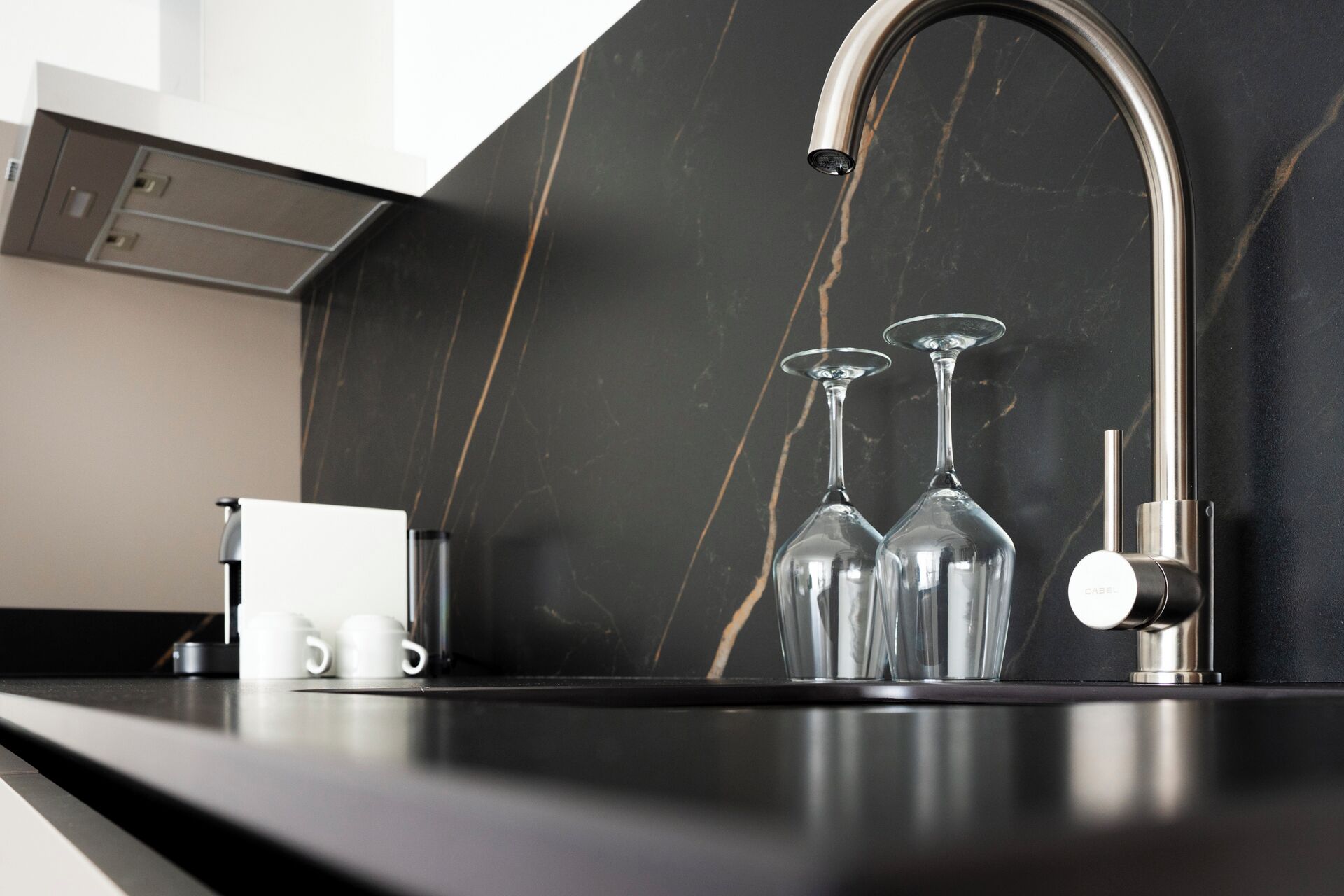 A modern kitchen with a black marble backsplash, stainless steel faucet, and two wine glasses on the counter.
