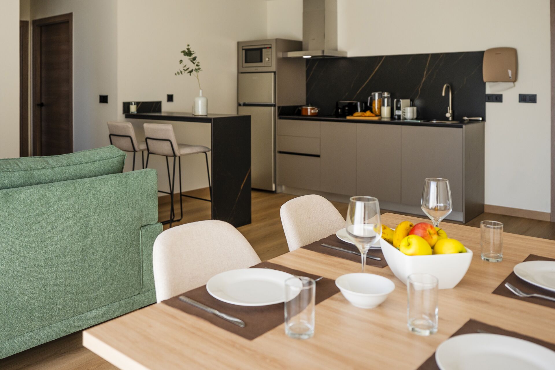 Un comedor moderno con una mesa de madera dispuesta para cuatro personas, un frutero y copas de vino.