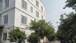 A multi-story building with a flat facade, several windows, and a paved area with trees and parked motorcycles. - Darpan Nikunj Rubystone Express (Vrindavan)