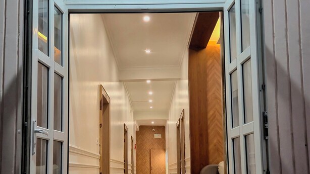 A hallway with open doors leading to rooms, a wooden floor, and a ceiling with recessed lighting. - Darpan Nikunj Rubystone Express (Vrindavan)