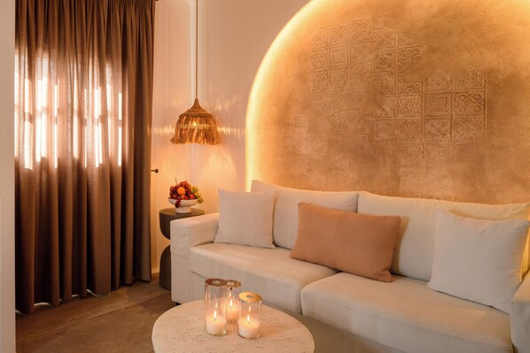 A modern living room with a white sofa, a round coffee table with candles, and a decorative wall. - Themis Goddess Cave Suites (Santorini)