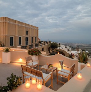 A terrace with wooden furniture, candles, and potted plants. - Themis Goddess Cave Suites (Santorini)