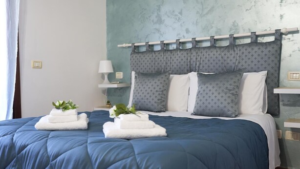 Ein ordentlich bezogenes Bett mit blauer Bettwäsche, weißen Kissen und einem dekorativen Kopfteil.