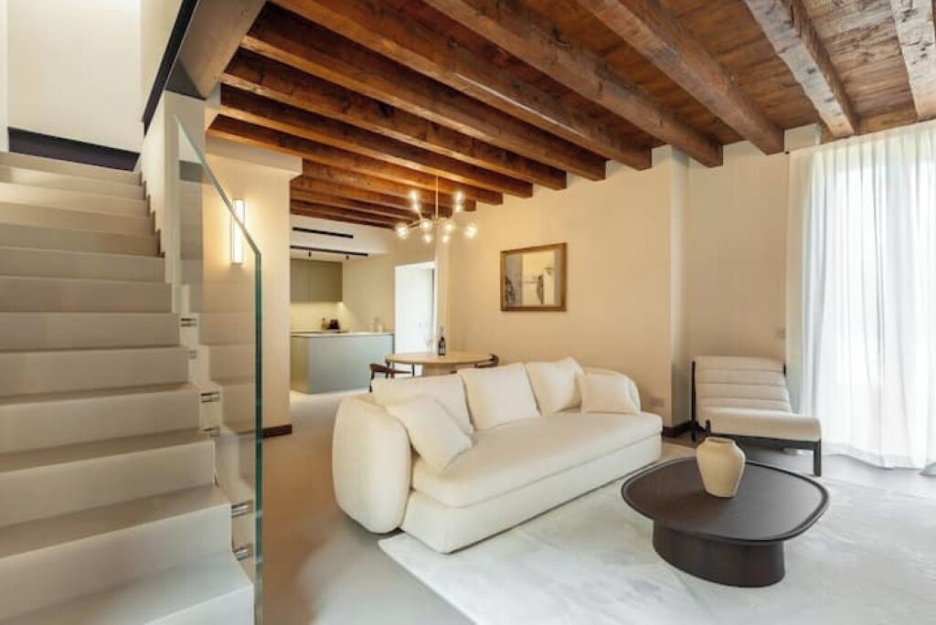 A modern living room with a white sofa, a coffee table, and a staircase with glass railings.