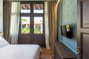 A bedroom with a bed, a dresser, a TV mounted on the wall, and a window with curtains. - Appartamento Brut (Iseo)