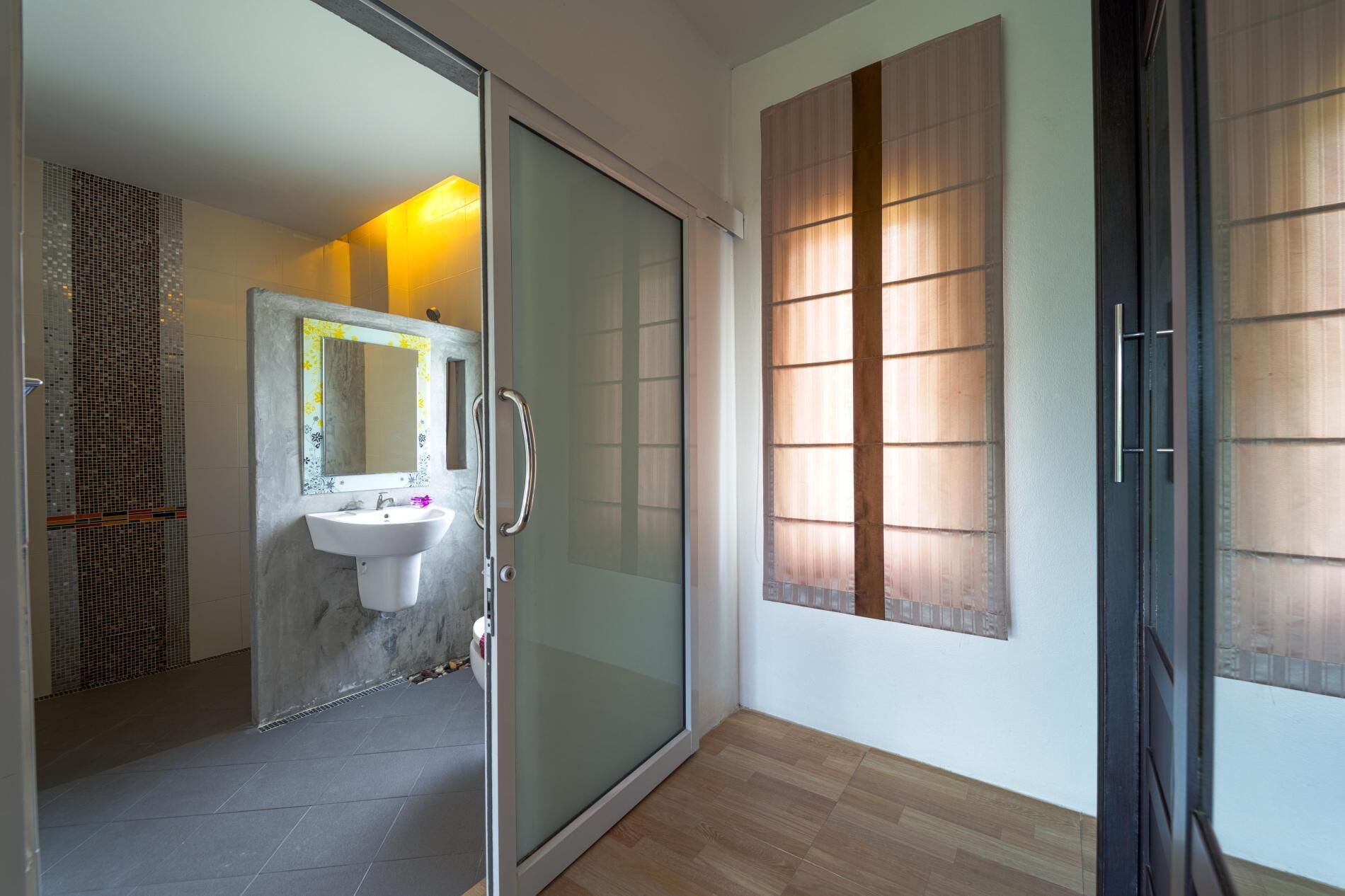 A modern bathroom with a glass shower door, a white sink, and a mirror with a decorative frame.