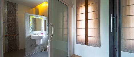 A modern bathroom with a glass shower door, a white sink, and a mirror with a decorative frame.