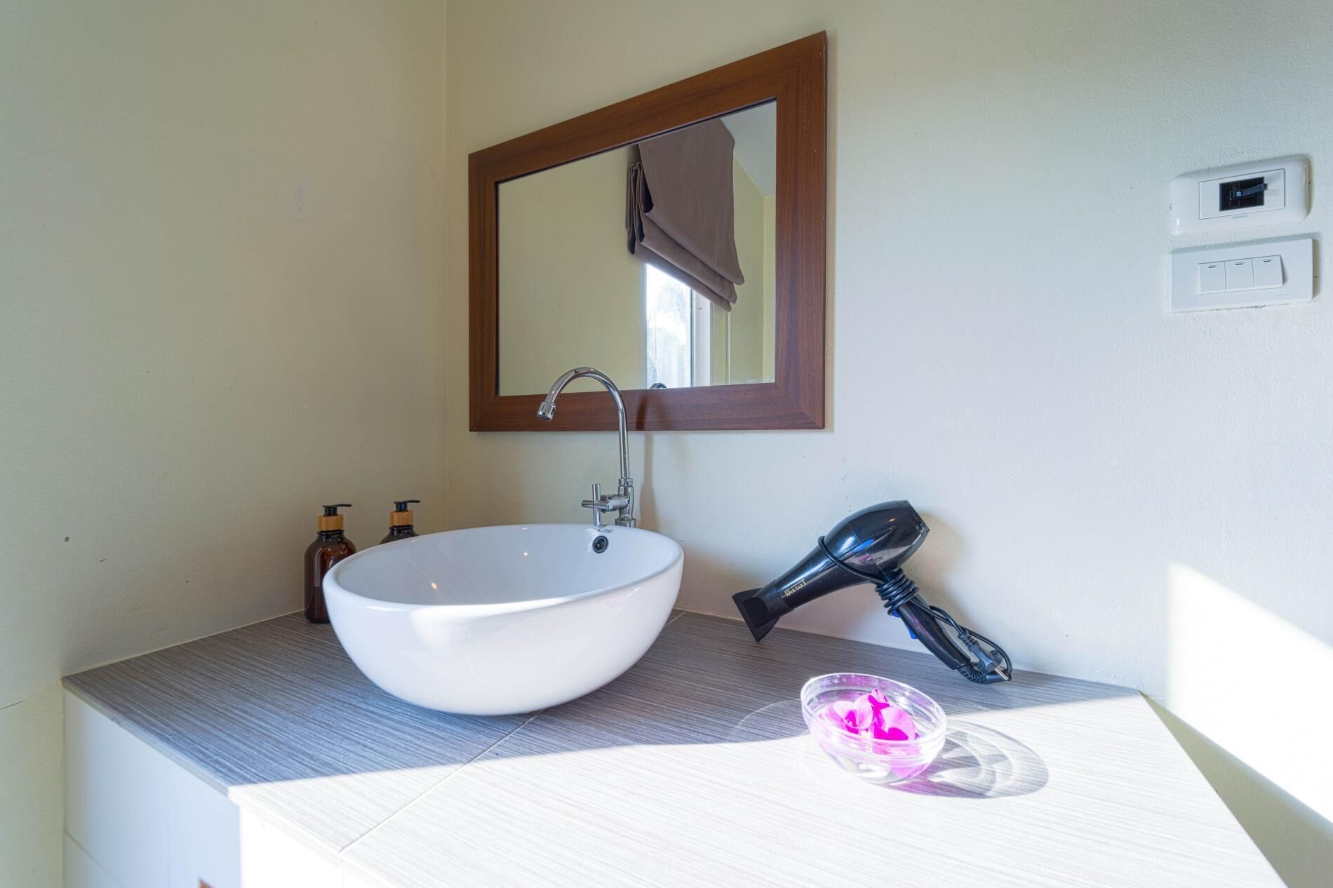 A bathroom with a white sink, a mirror, and a hairdryer on the counter.