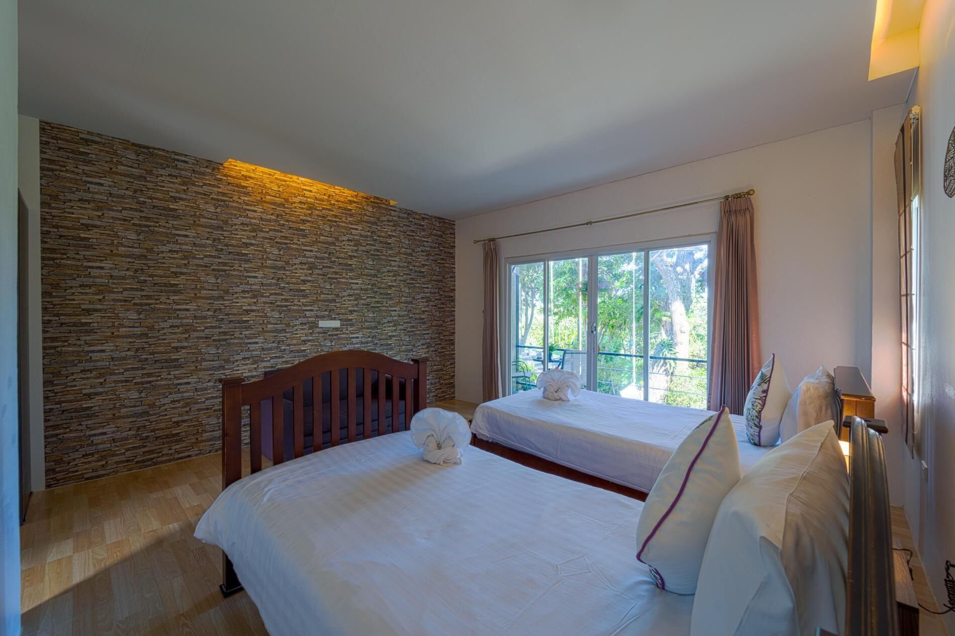 A hotel room with a stone wall, a large window with curtains, a bed, and a bedside table.