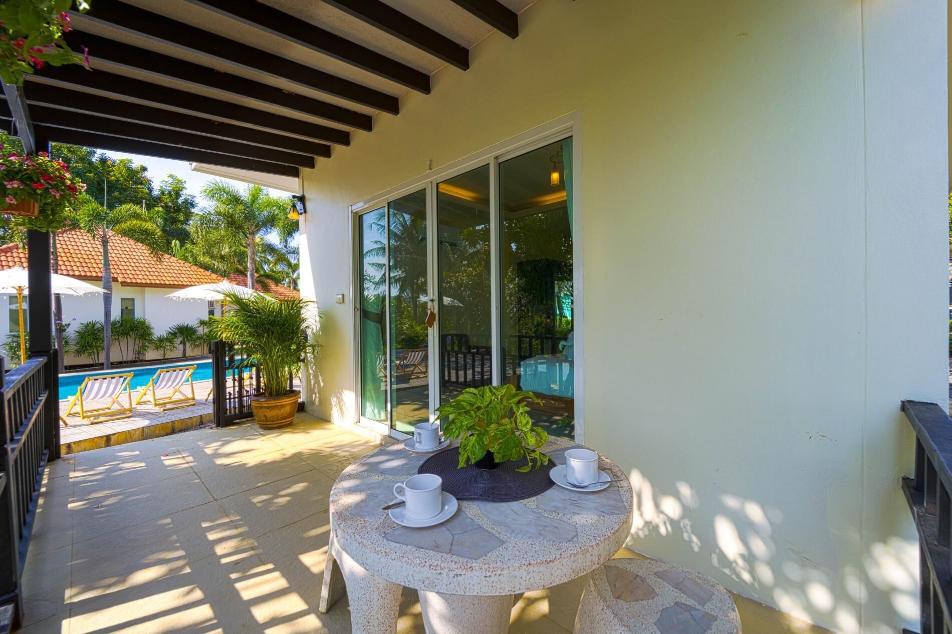 Um alpendre coberto com piscina, uma mesa com chávenas e uma planta, e vista para a área da piscina.