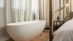 A modern bathroom with a large freestanding bathtub, a small round table with a bottle, and a curtain partially drawn. - Suite..... (Iseo)
