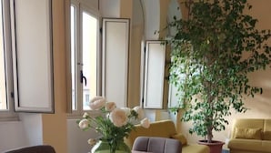 A dining area with a wooden table, chairs, a vase with flowers, a yellow sofa, and a large potted plant.
