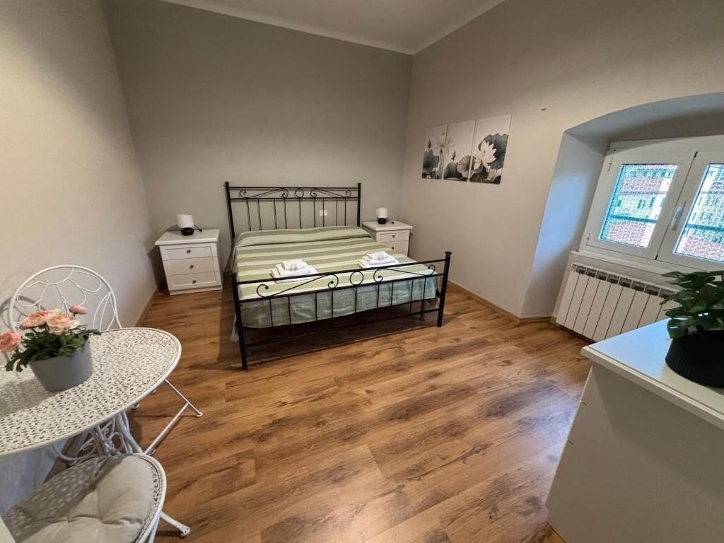 Un dormitorio con cama, mesitas de noche, una pequeña mesa con una silla y un radiador.