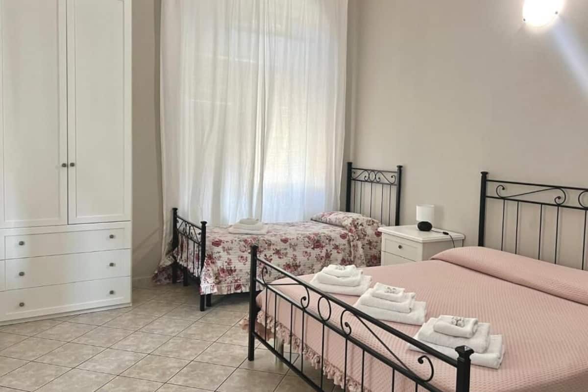 A bedroom with a bed, two bedside tables, a wardrobe, and a window with sheer curtains.