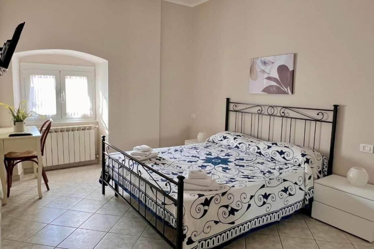 A bedroom with a bed, a desk, a chair, a radiator, and a window.