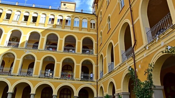 A multi-story building with a yellow facade, multiple balconies, and arched windows.