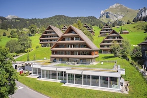 A cluster of chalet-style buildings with a modern annex, set in a lush green valley with mountains in the background. - Reka-Feriendorf Wildhaus (Wildhaus-Alt St. Johann)