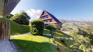 Une maison moderne, dotée d’un toit en pente, entourée d’une végétation luxuriante et offrant une vue dégagée sur les montagnes lointaines.