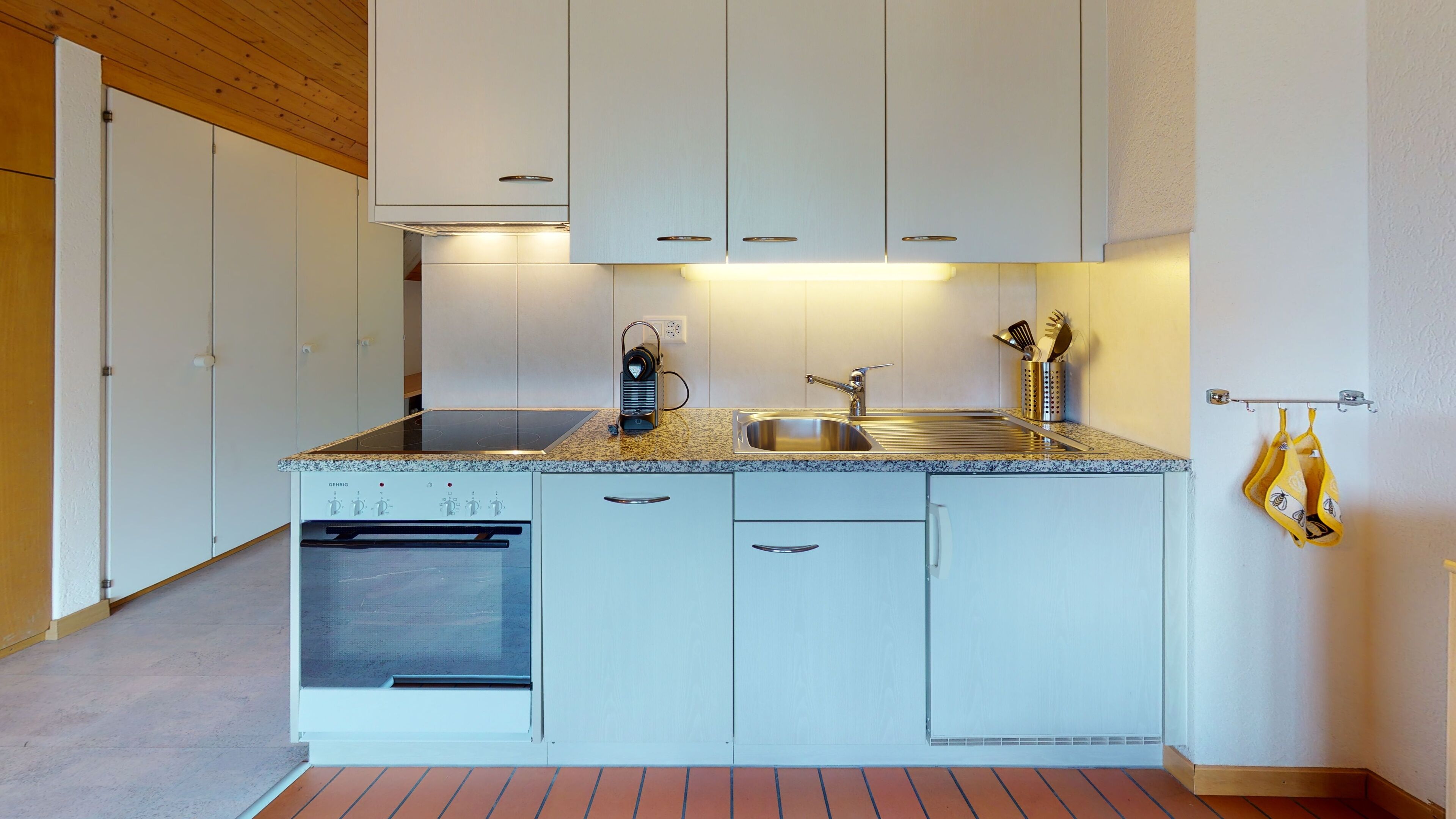 A compact kitchen with white cabinets, a built-in oven, a stainless steel sink, and a granite countertop.