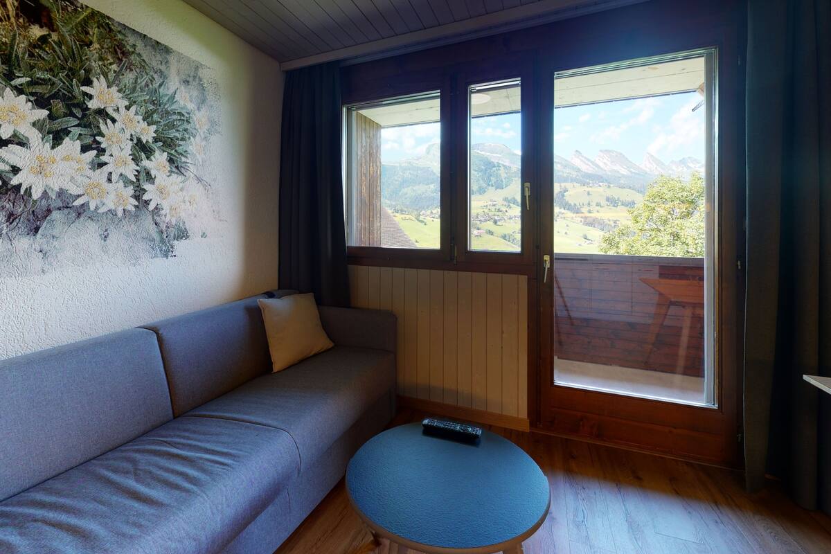 Ein Zimmer mit einer Couch, einem kleinen runden Tisch und einem großen Fenster mit Bergblick.