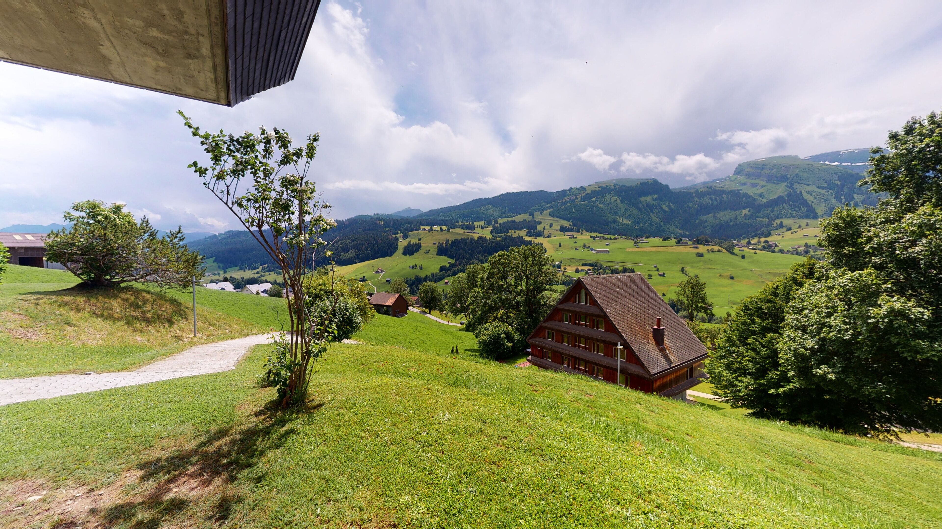 A rural landscape with a traditional wooden house, a dirt path, and rolling hills in the background.