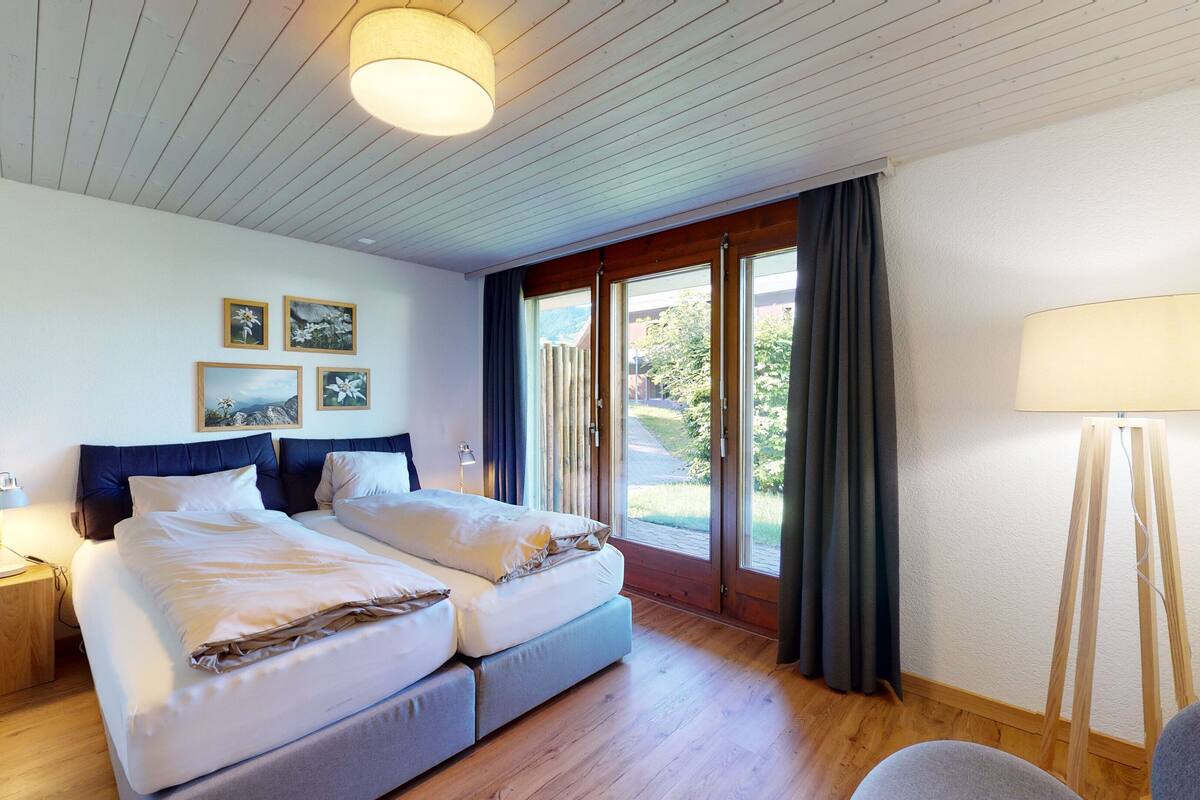 Ein Hotelzimmer mit Doppelbett, Nachttisch mit Lampe, Stehlampe und drei gerahmten Bildern an der Wand.