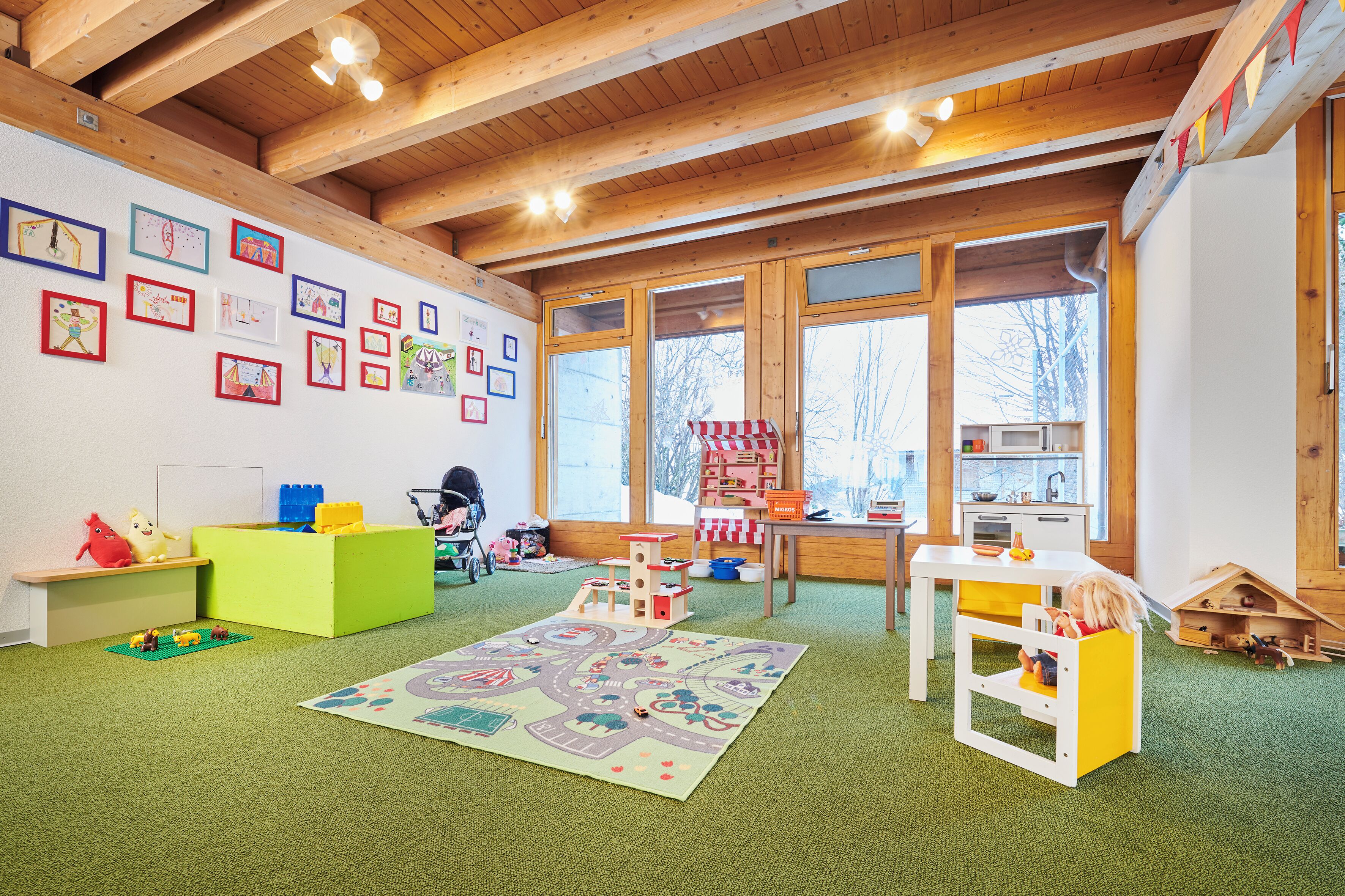 A spacious room with wooden beams, large windows, and a play area with toys and a play mat.