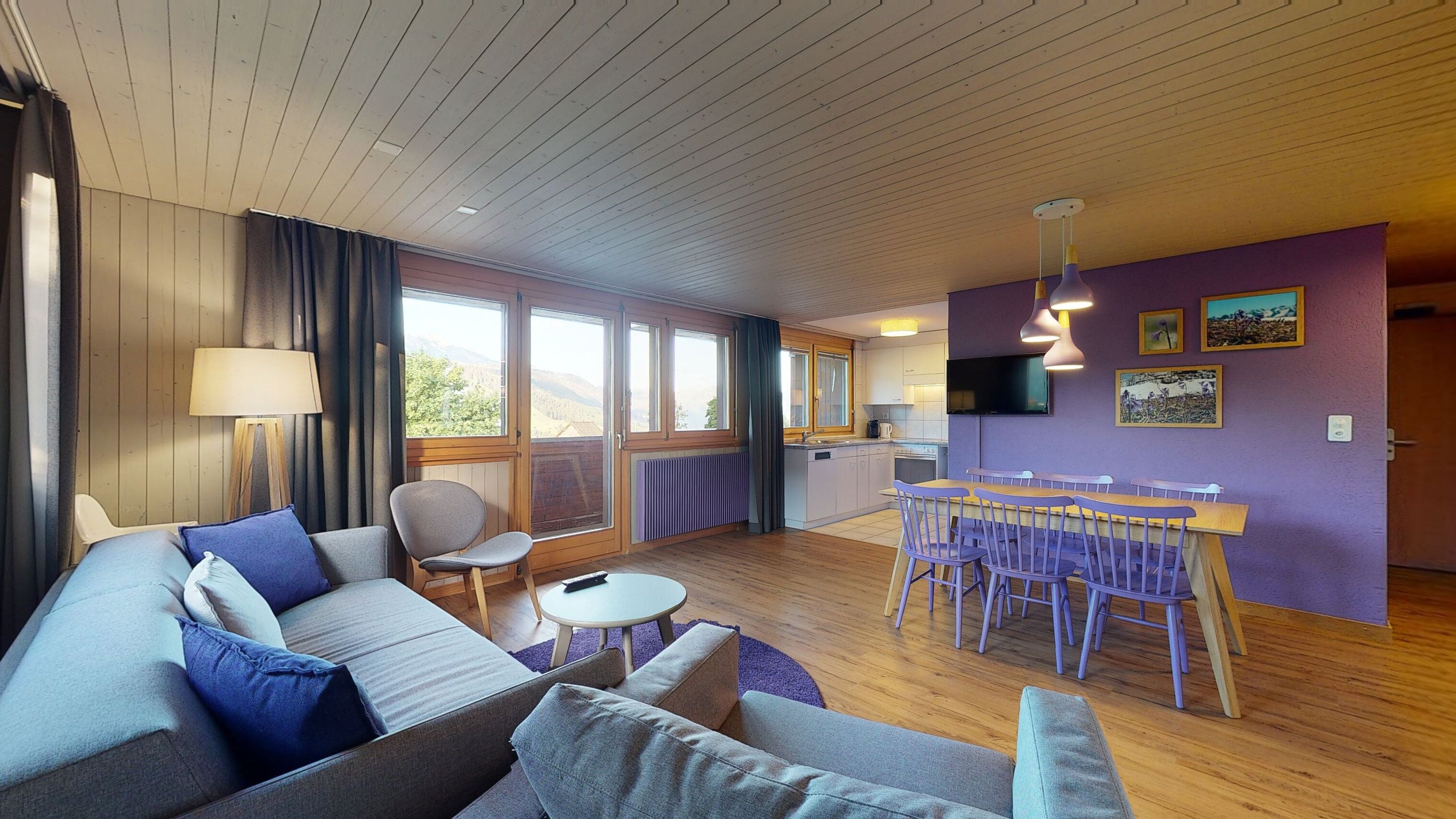 A modern living room with a sofa, chairs, a dining table, and a kitchen area with a TV.