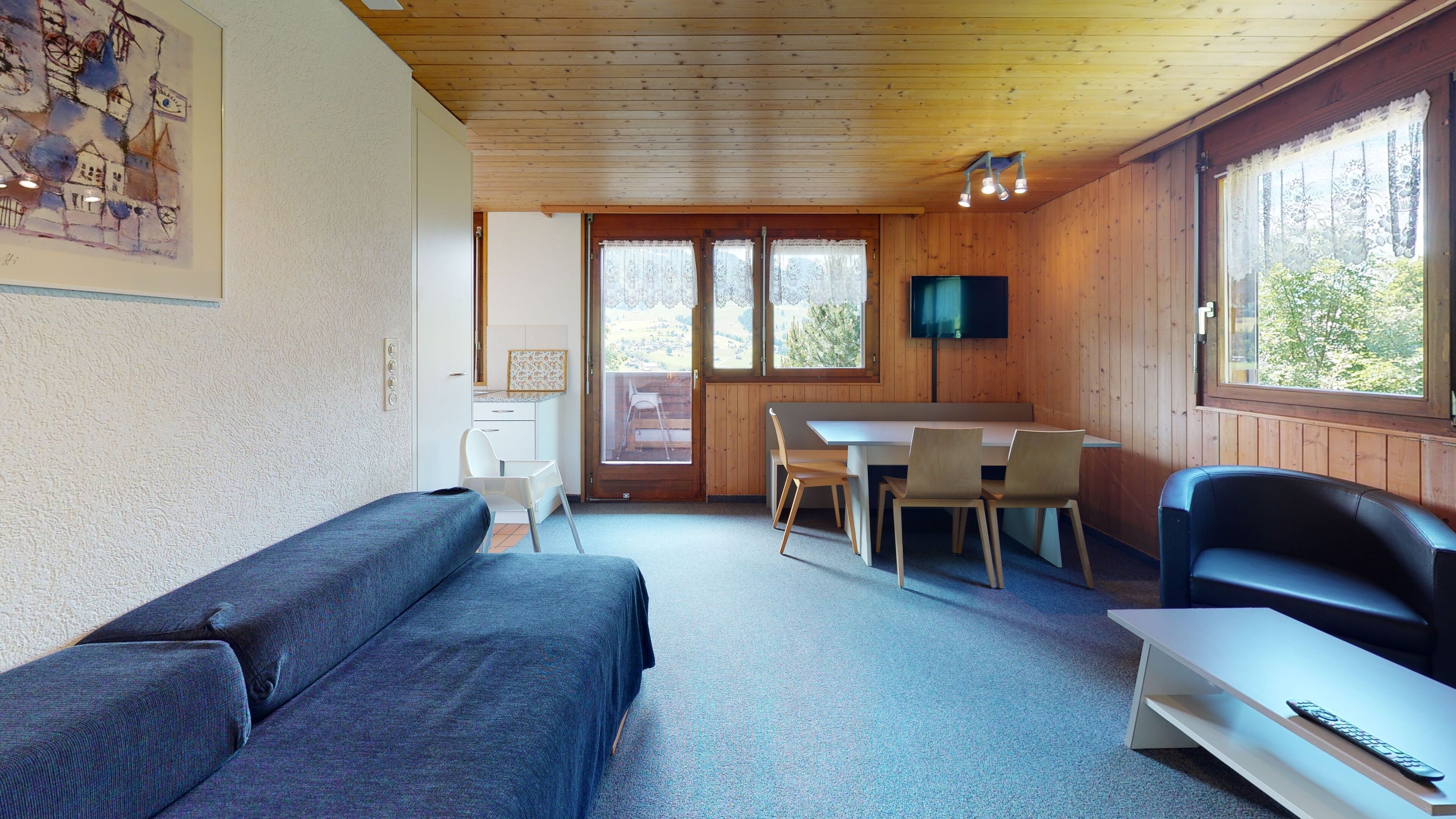 Ein gemütliches Blockhaus-Interieur mit Holzbalkendecke, einer Essecke mit Tisch und Stühlen, einer Couch und einem an der Wand befestigten Fernseher.