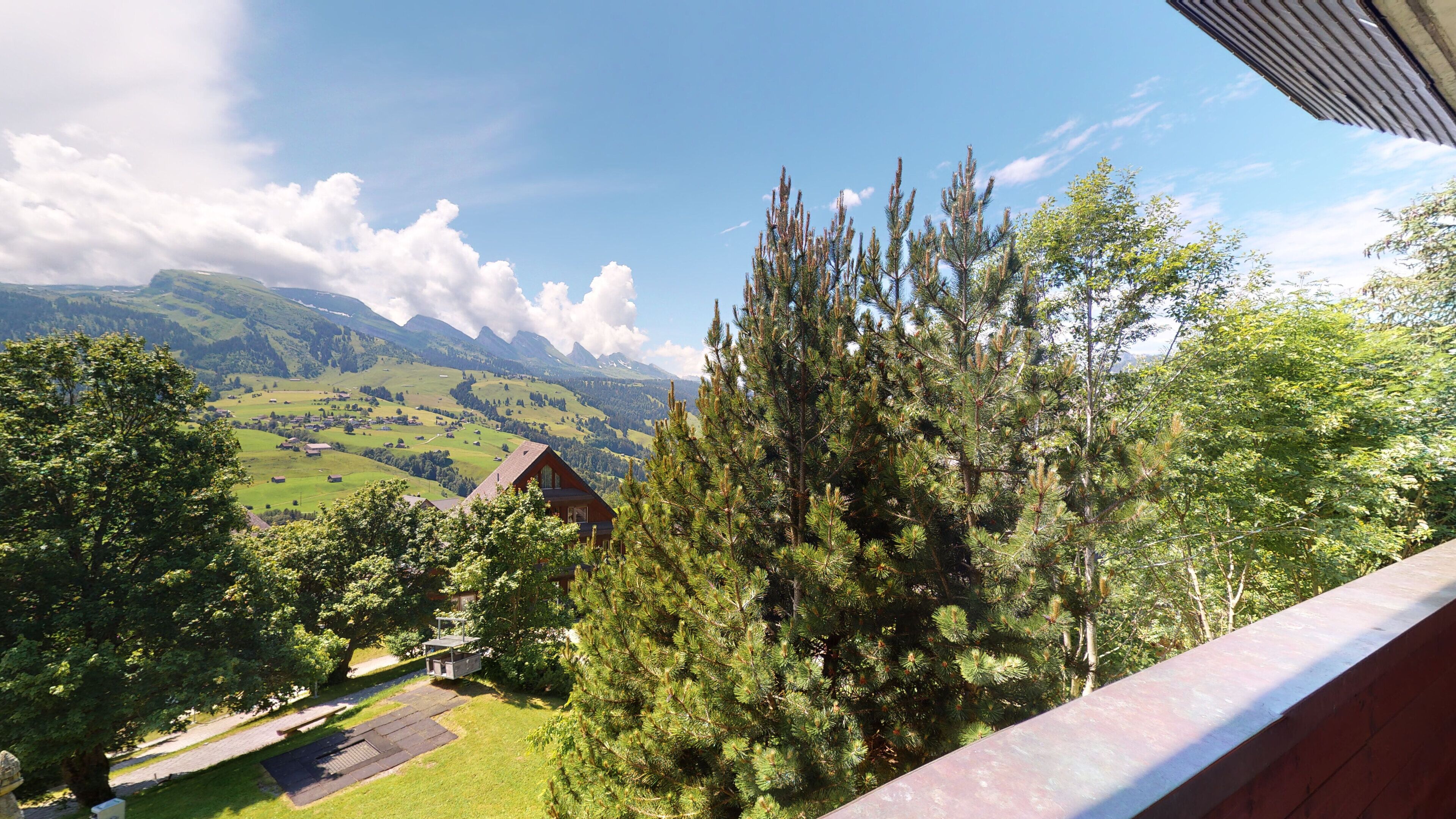 Blick auf Berge mit einem Haus und einem großen Baum im Vordergrund.