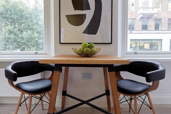 A dining area with a table, two chairs, a bowl of fruit, and a framed artwork on the wall. - 2VH Virginia House, 31 Bloomsbury Way by City Living London (London)