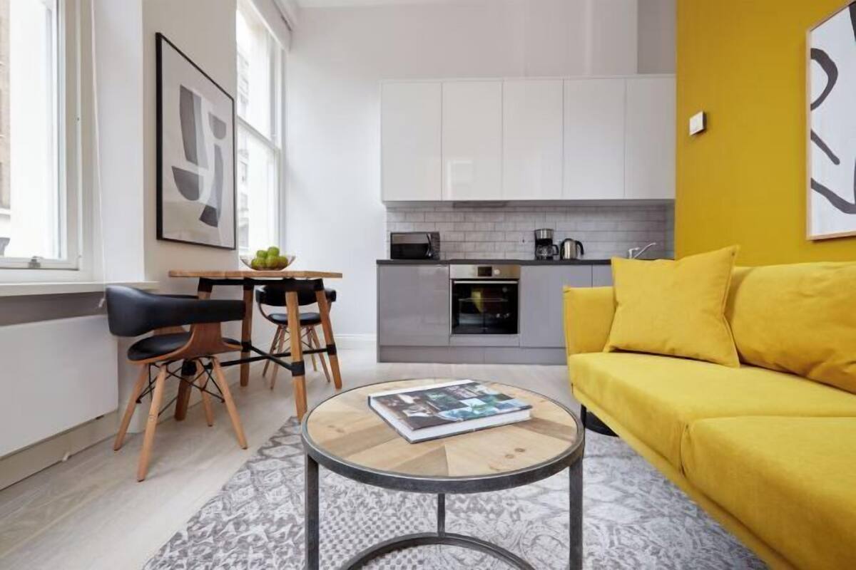 A modern kitchen with white cabinets, a dining area with a table and chairs, and a yellow sofa.