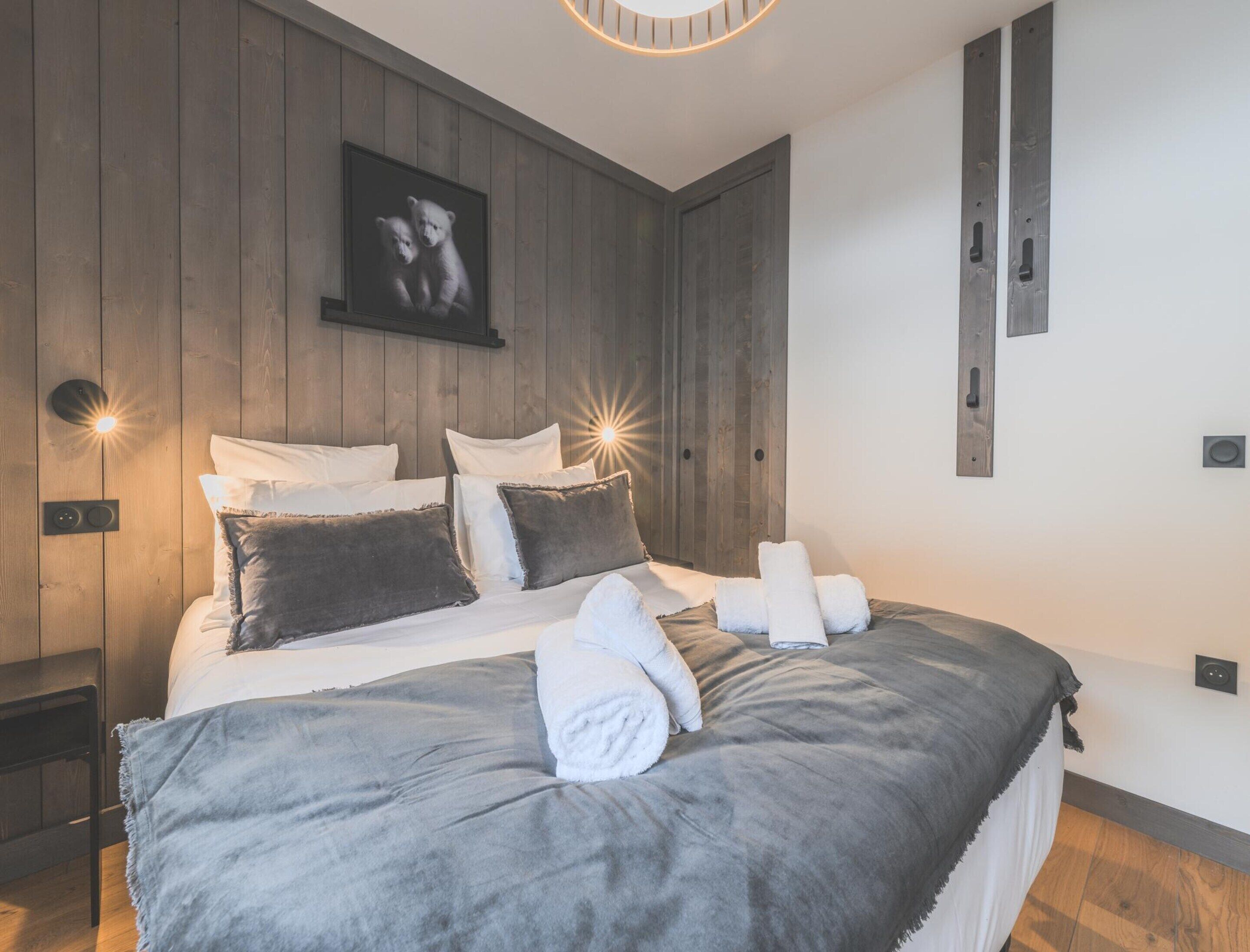 Ein modernes Schlafzimmer mit einer Wandpaneele aus Holz, einem großen Bett mit weißer und grauer Bettwäsche, zwei Nachttischlampen und einem gerahmten Bild über dem Bett.