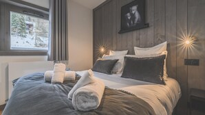 Ein modernes Schlafzimmer mit einem großen Bett, grauer Bettwäsche und einem gerahmten Bild an der Wand.