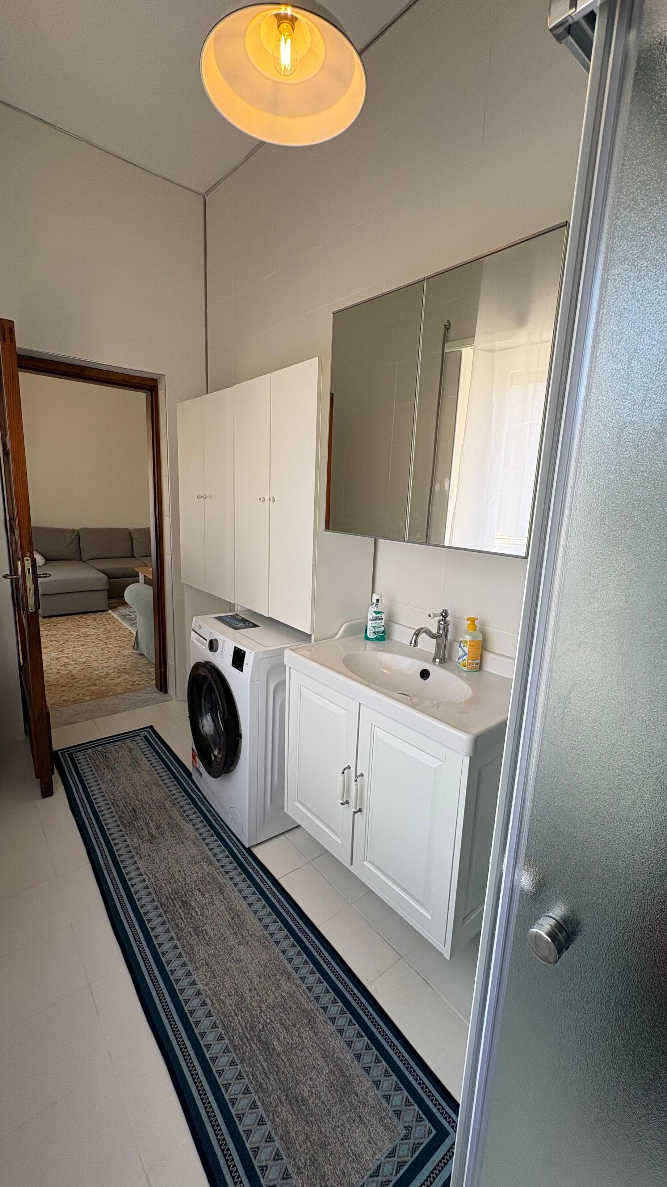 Ein kleines, modernes Badezimmer mit Waschmaschine, Waschbecken und Spiegel.