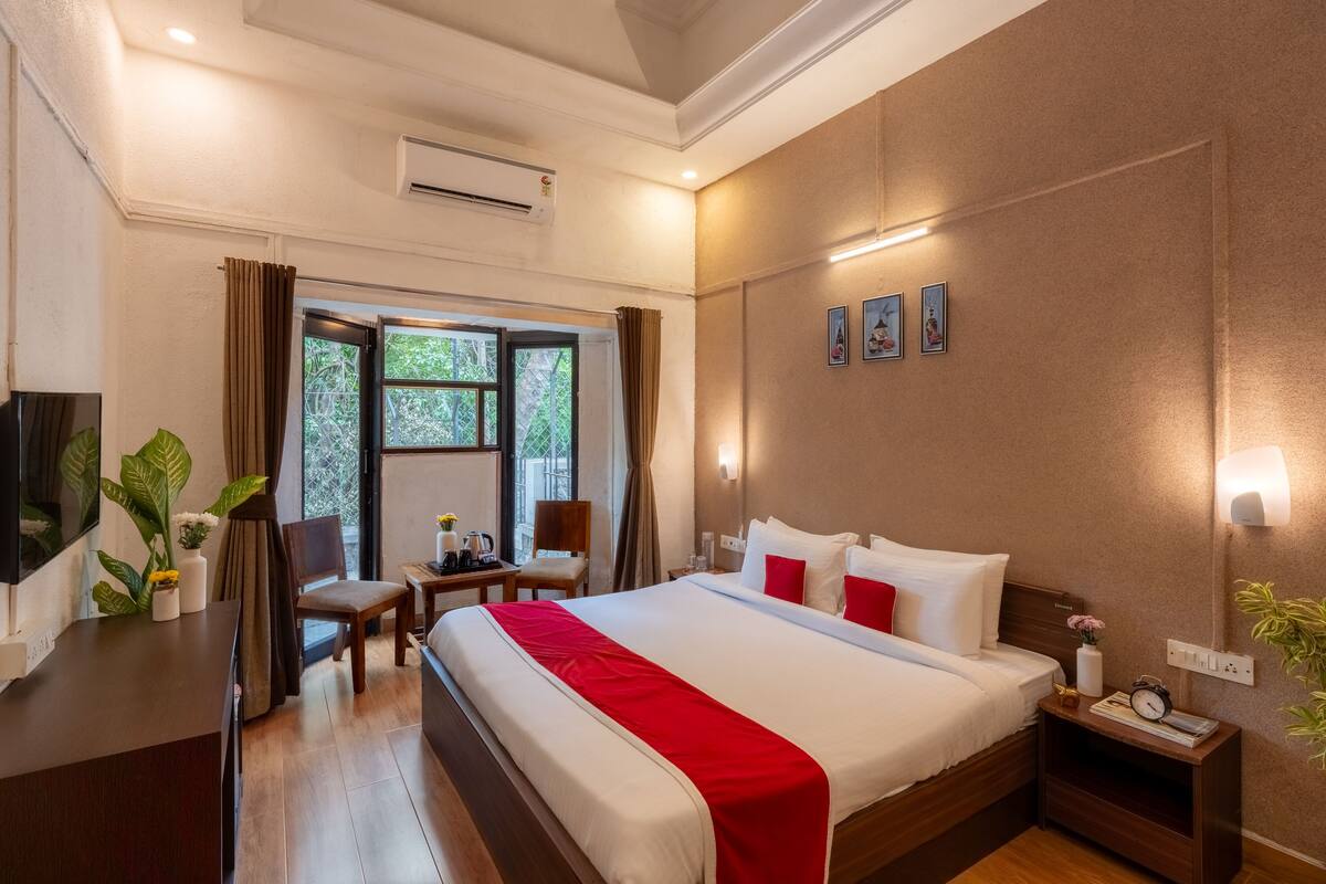 A hotel room with a bed, bedside table, desk, chair, and a window with curtains.
