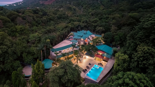 A resort with multiple buildings, a swimming pool, and lush surrounding vegetation. - Velvet County Resort (Lonavala)