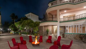 A courtyard with a fire pit surrounded by red chairs, a stone building with balconies, and a staircase leading to an upper level. - Velvet County Resort (Lonavala)