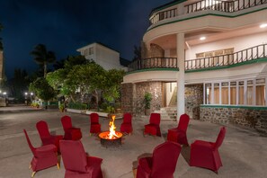 Une cour avec un foyer entouré de chaises rouges, un bâtiment en pierre doté de balcons et un escalier menant à un étage supérieur.
