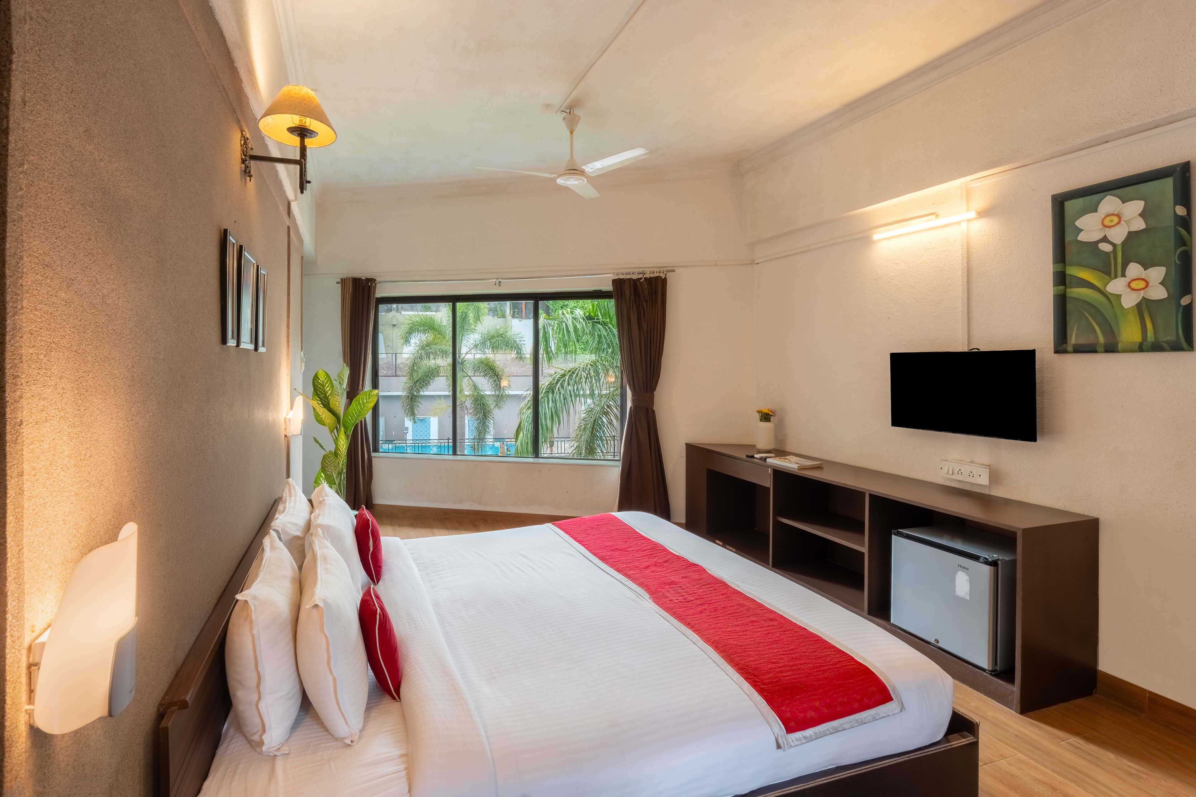Ein Hotelzimmer mit Bett, Schreibtisch, Fernseher und einem Fenster mit Blick auf Palmen.