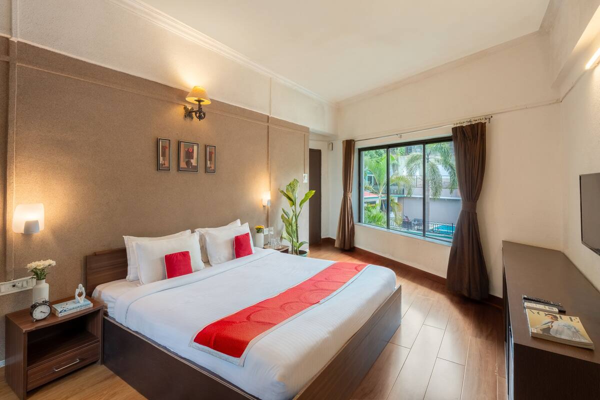 A hotel room with a large bed, bedside lamps, a TV, and a window with curtains.