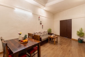 A dining area with a wooden table, chairs, a fruit bowl, and a sofa with floral cushions. - Velvet County Resort (Lonavala)