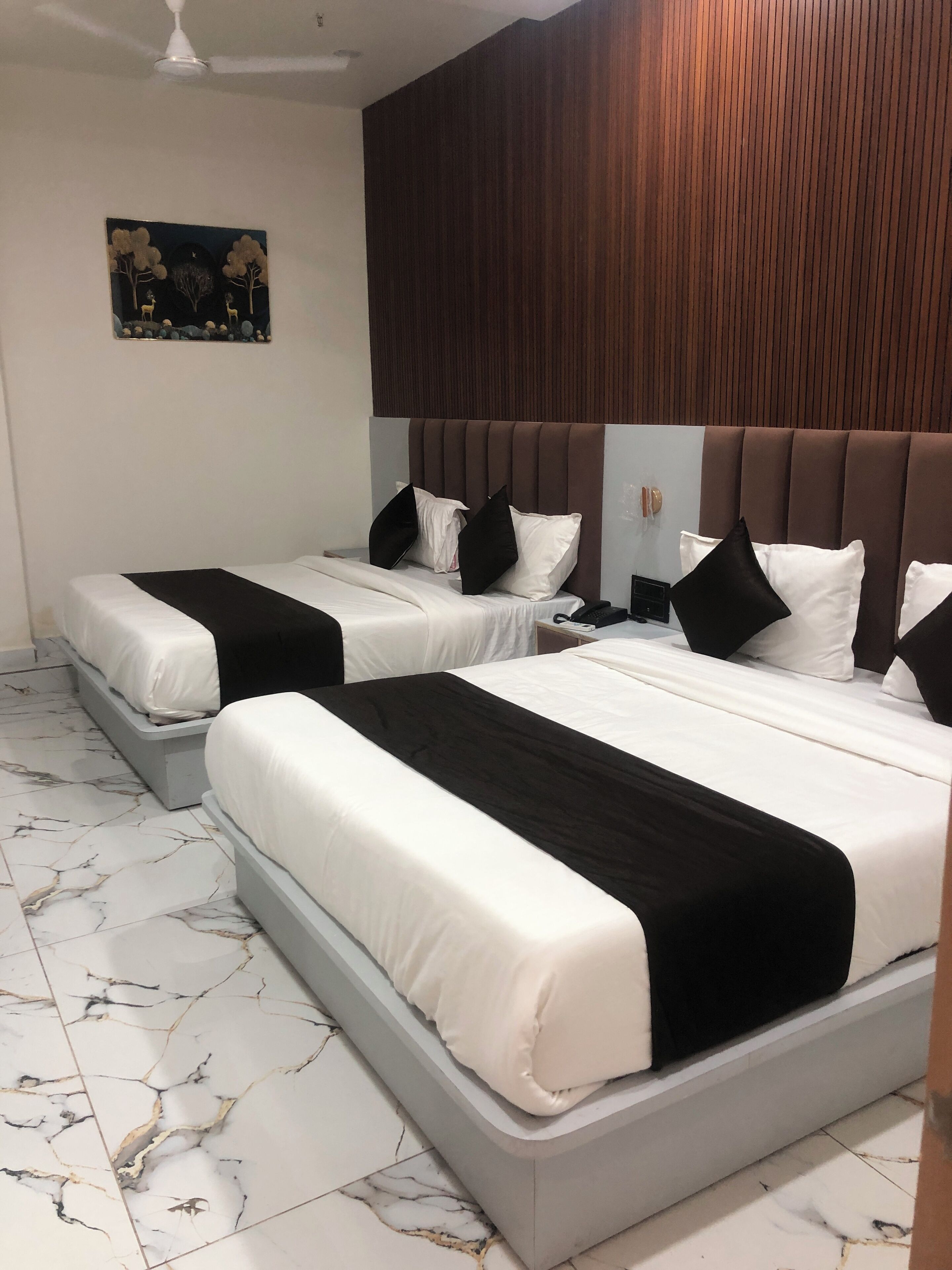 A hotel room with two beds, marble flooring, a wooden headboard, and a painting on the wall.