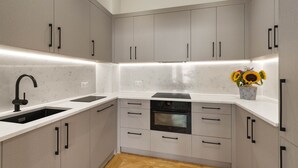 A modern kitchen with grey cabinets, black handles, a black faucet, and a built-in oven. - Kensington Apartment | Hyde Park, Portobello, Royal Albert Hall (London)